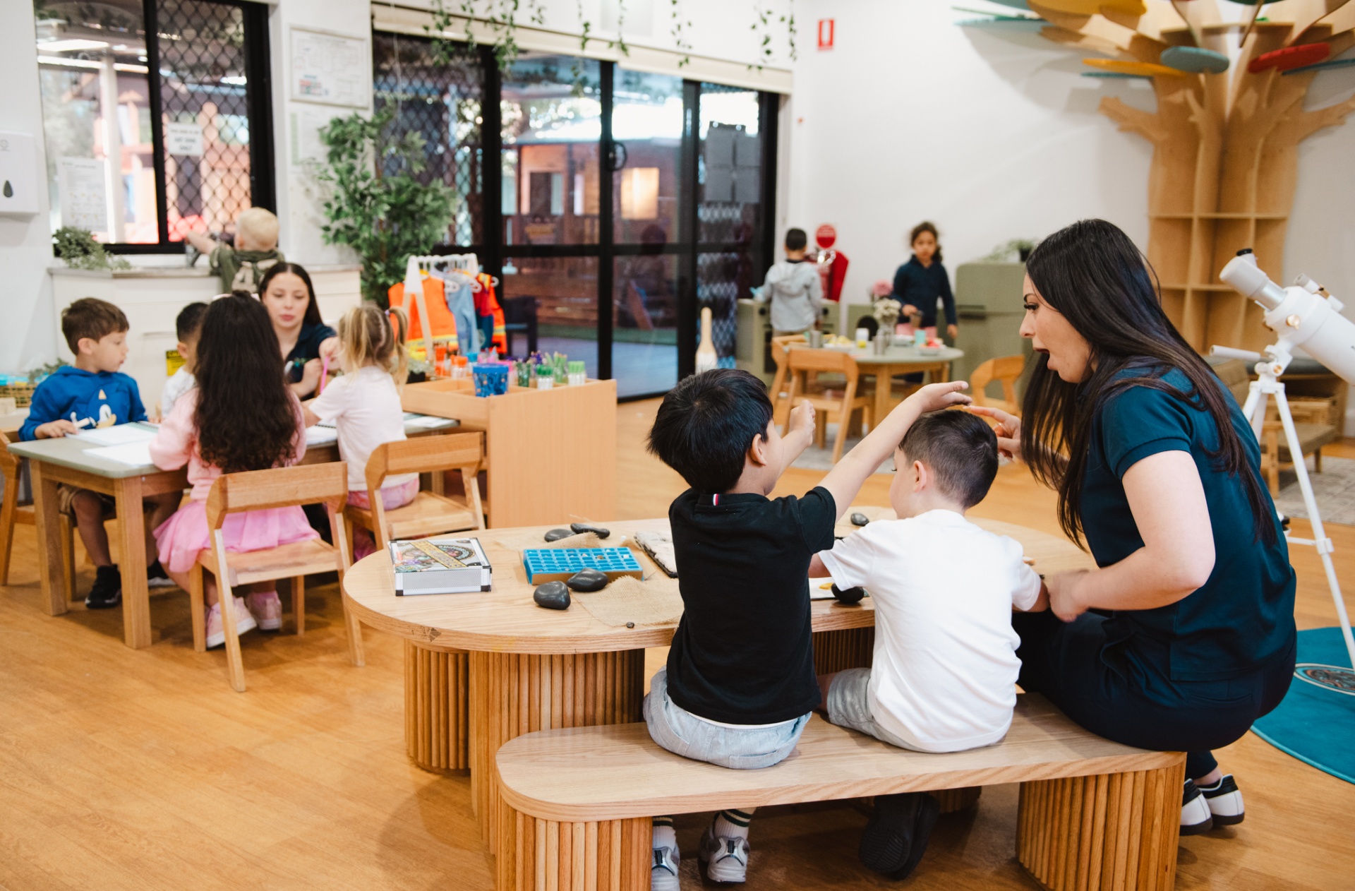 Educator engaging with toddlers at a nature play table